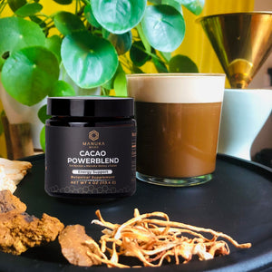 A jar of Manuka Mana's Cacao Powerblend is pictured next to a cup of  coffee.