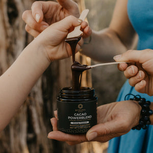 For the energy bundle, a jar of Cacao Powerblend is pictured with two sets of hands using spoons to take a scoop of the powerblend.