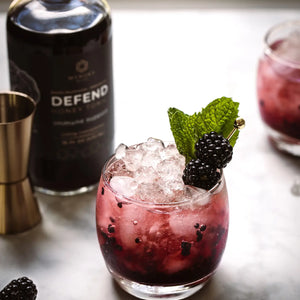 A glass of DEFEND, Manuka Mana's red reishi tonic, is pictured with blackberry garnish.
