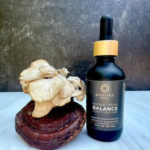 A bottle of Maitake Reishi Balance Honey Tincture is pictured next to maitake and reishi mushrooms.