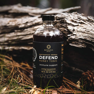 A glass bottle of Defend, Manuka Mana's red reishi tonic, is pictured in nature in front of a log.