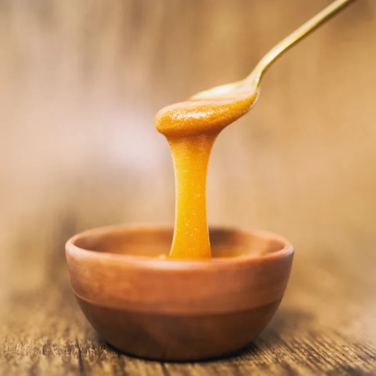 A spoon is taking a scoop of manuka honey from a bowl.