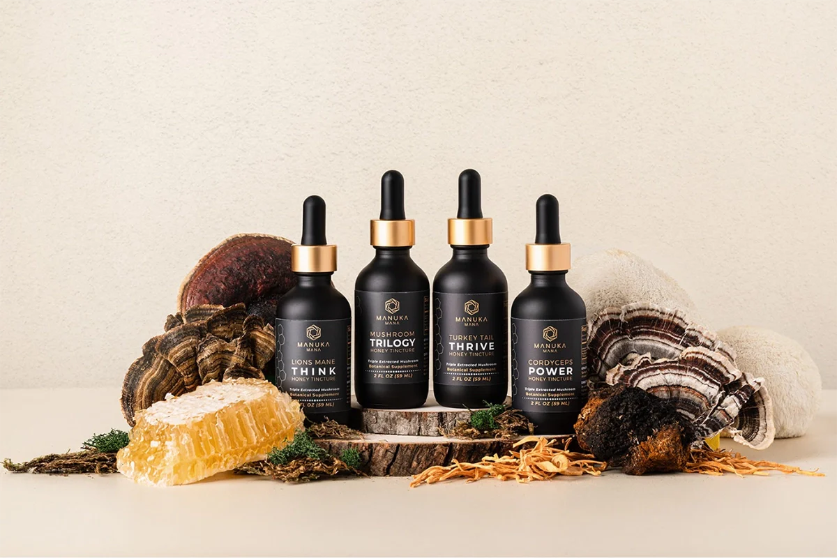 A picture of Manuka Mana's tincture-based mushroom supplement jars are pictured with dried mushrooms and a honeycomb.