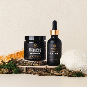 The Manuka Mana Brain Bundle of the Royal Boost Honeyblend and the Lion's Mane tincture is shown surrounded by a honeycomb and a lion's mane mushroom while sitting on top of two wooden cuts from a tree stump. 