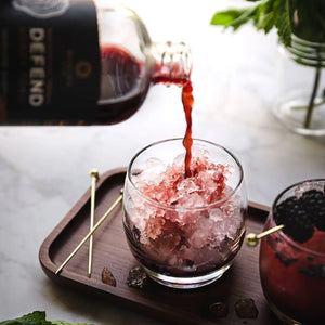 A glass bottle of Manuka Mana's red reishi tonic is being poured into a glass with ice. 