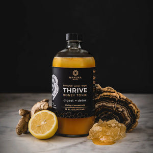 A bottle of Manuka Mana's turkey tail tonic is surrounded by its ingredients--turkey tail mushrooms, lemon, ginger, and manuka honey.